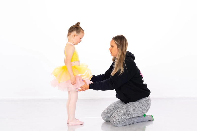 Child being assisted by an instructor in a ballet dance class